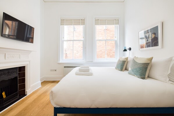 A bedroom with a large bed, a fireplace, and two windows with blinds.
