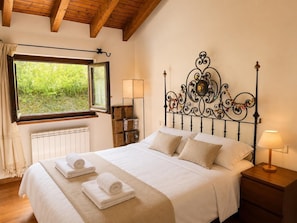 A bedroom with a bed, a window, a radiator, a bedside table with a lamp, and a decorative metal headboard.