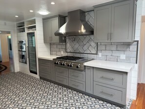 A kitchen with grey cabinets, a stainless steel range hood, a built-in oven, and a patterned tile floor.