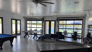 Un tavolo da biliardo, un divano blu, un tavolo da pranzo con sedie e una ventola a soffitto in una stanza con ampie finestre.