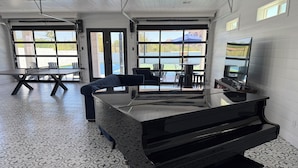 Una stanza con un pianoforte, un tavolo, sedie e ampie finestre che danno su un panorama.