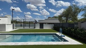 Una piscina con un canestro da basket, circondata da un prato curato e una recinzione.