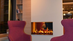 A modern room with a fireplace, two purple chairs, a bookshelf, and a small table with a vase. - Boutique Hotel Moselgarten (Bullay)