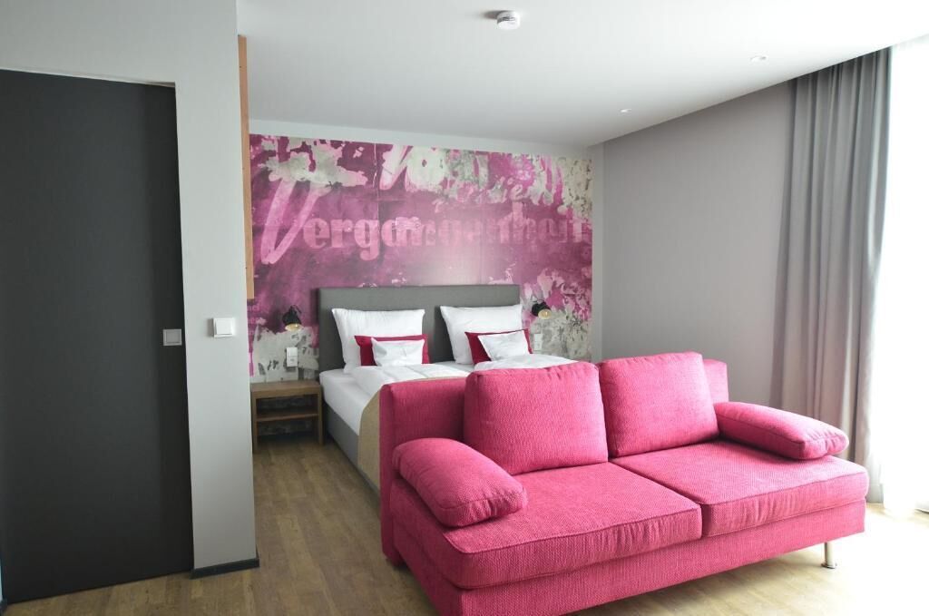 A modern bedroom with a bed, a pink sofa, and a wall with floral artwork.