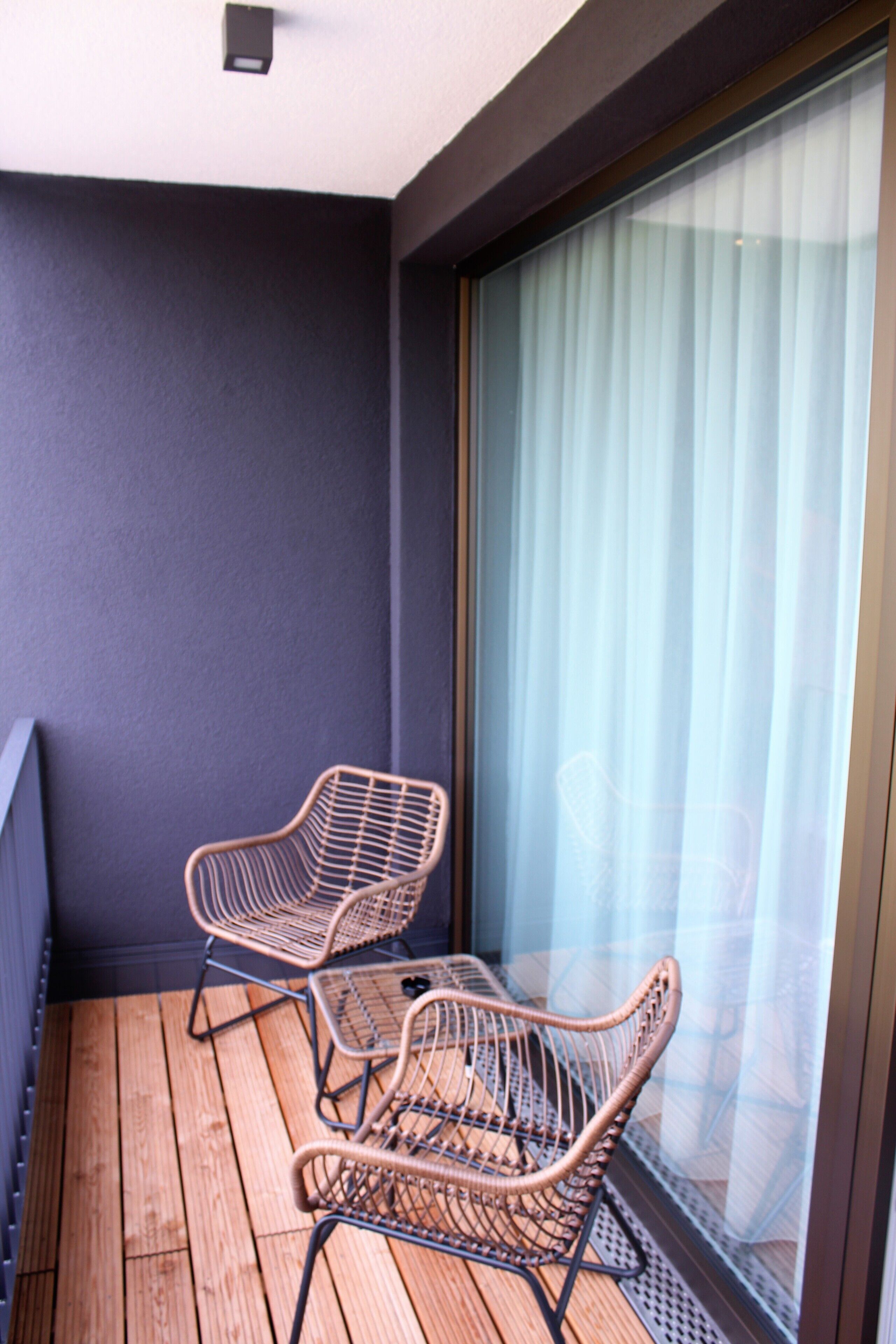 A balcony with two wicker chairs and a wooden floor.
