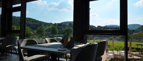 A modern dining area with large windows, a view of a green landscape, and outdoor seating.