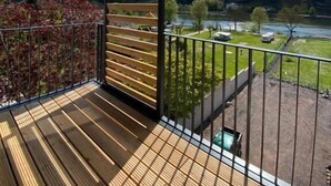 A wooden deck with a metal railing, overlooking a river and hills. - Boutique Hotel Moselgarten (Bullay)