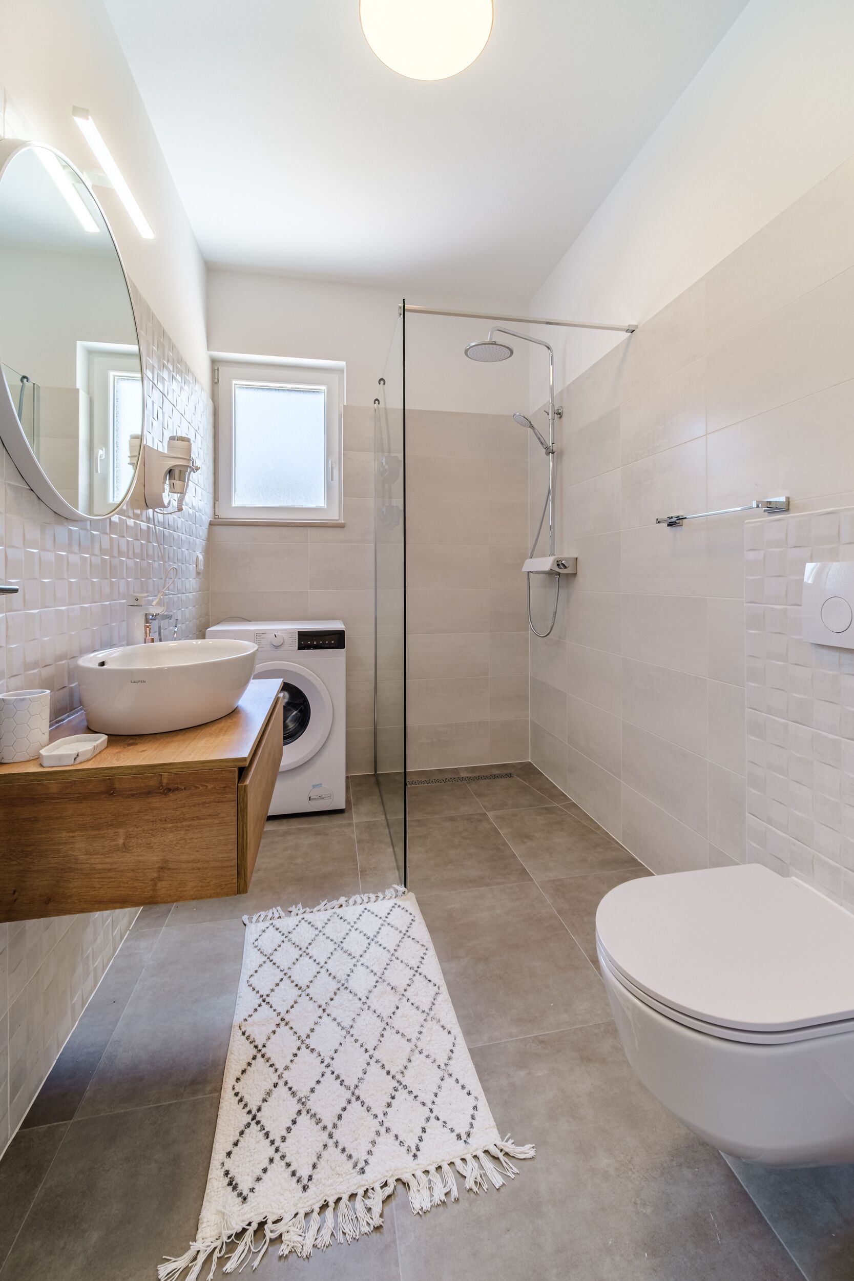 A modern bathroom with a sink, washing machine, toilet, and shower.
