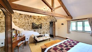 Une chambre avec un mur en pierre, des poutres en bois, un lit, un canapé, un bureau et une fenêtre avec des rideaux.