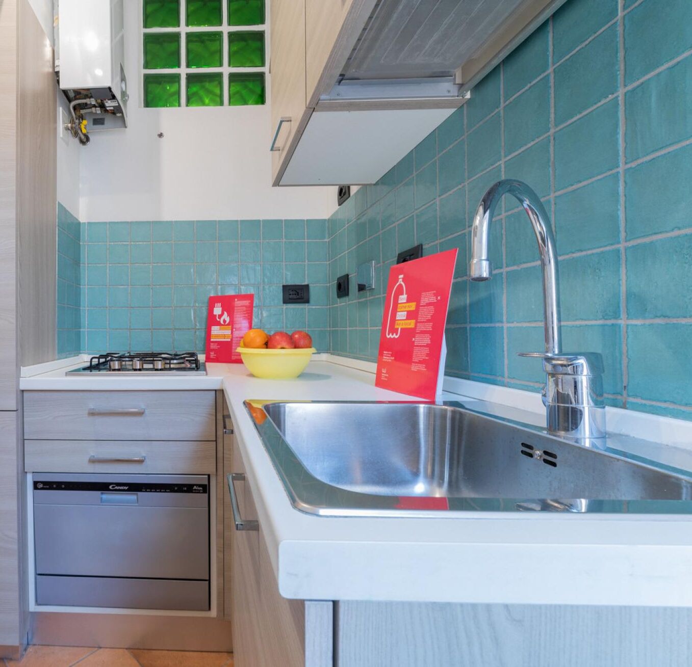 A kitchen with teal tiles, a stainless steel sink, a gas stove, and a dishwasher.