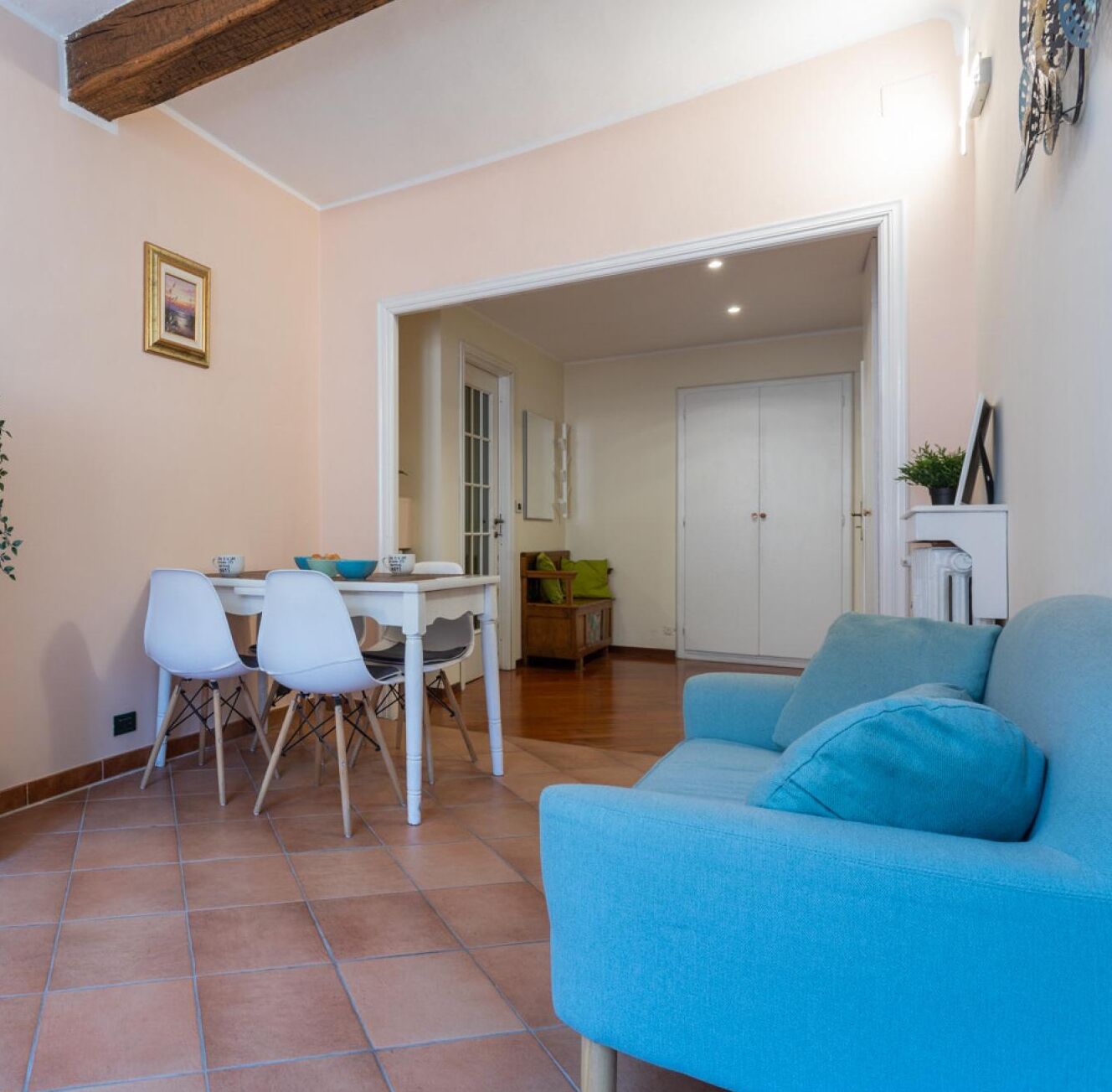 A living room with a blue sofa, a dining area with a table and chairs, and a door leading to another room.