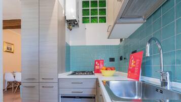 Una cocina moderna con estufa a gas, lavavajillas y un lavabo. Hay un bol de fruta en la encimera y un cartel rojo con texto.