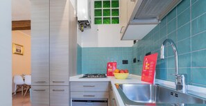 A modern kitchen with a gas stove, dishwasher, and a sink. There is a bowl of fruit on the counter and a red sign with text.