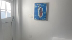 Una habitación con una puerta blanca, un felpudo con diseño de corazón, un cuadro de un pájaro y un banco rosa.