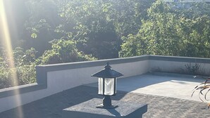 Un farol de piedra en una azotea, rodeado de un área pavimentada y vegetación.