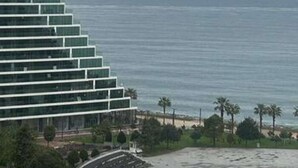 Een modern hotel met een meerlaagse structuur, uitzicht op het strand en palmbomen op de voorgrond.
