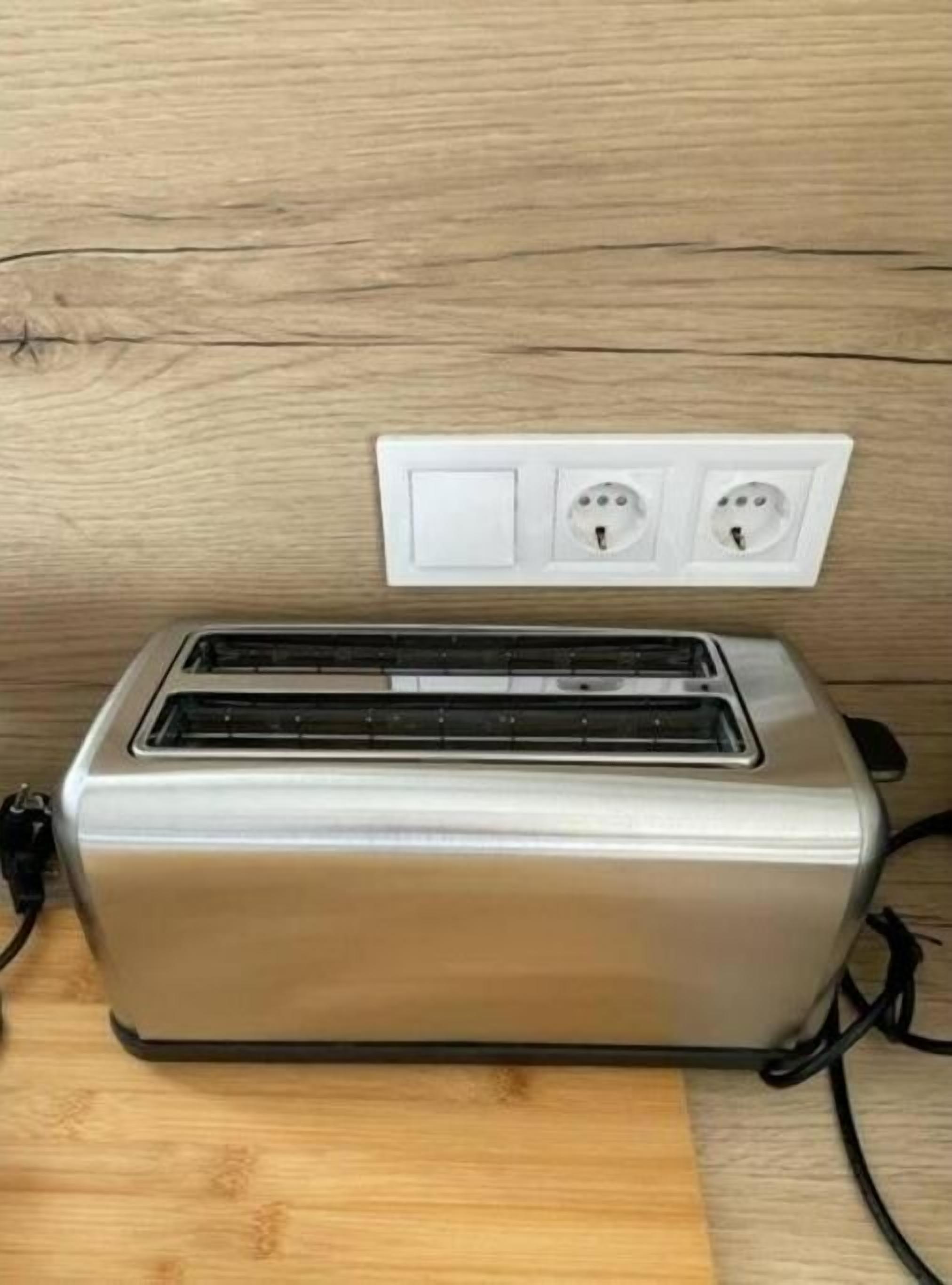 Ein silbernes Toaster auf einer Holztischplatte, darüber eine Steckdose.