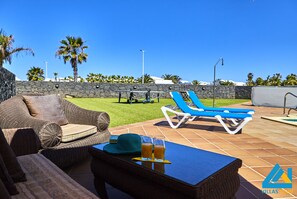 Relax in style with a comfortable wicker sofa and lounge chairs amidst a serene lawn and stone wall.