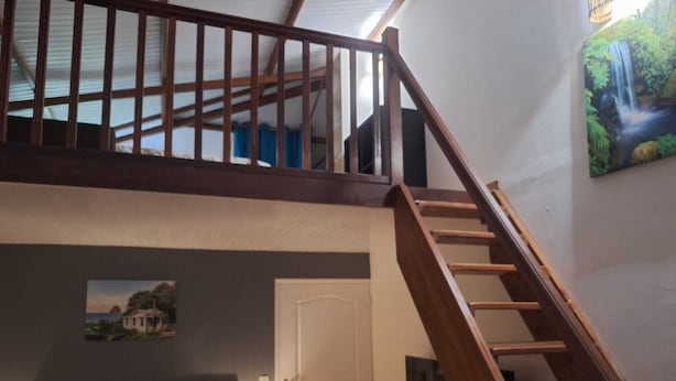 A bedroom with a bed, a nightstand, a TV mounted on the wall, and a staircase leading to an upper level. - A quiet gîte in the heart of nature (Lamentin)