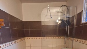 A small bathroom with a shower, toilet, and a wooden shelf. - A quiet gîte in the heart of nature (Lamentin)
