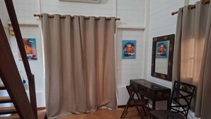 A room with a wooden staircase, a dining table with chairs, a window with beige curtains, and two wall-mounted paintings. - A quiet gîte in the heart of nature (Lamentin)