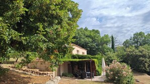Een rustiek huis met een overdekte patio, omringd door groen en een stenen muur.