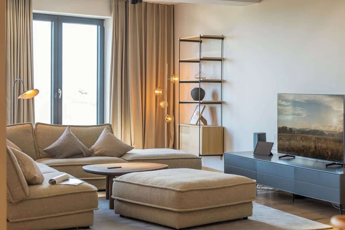 Een moderne woonkamer met een bank, een voetenbankje en een televisie op een meubel.