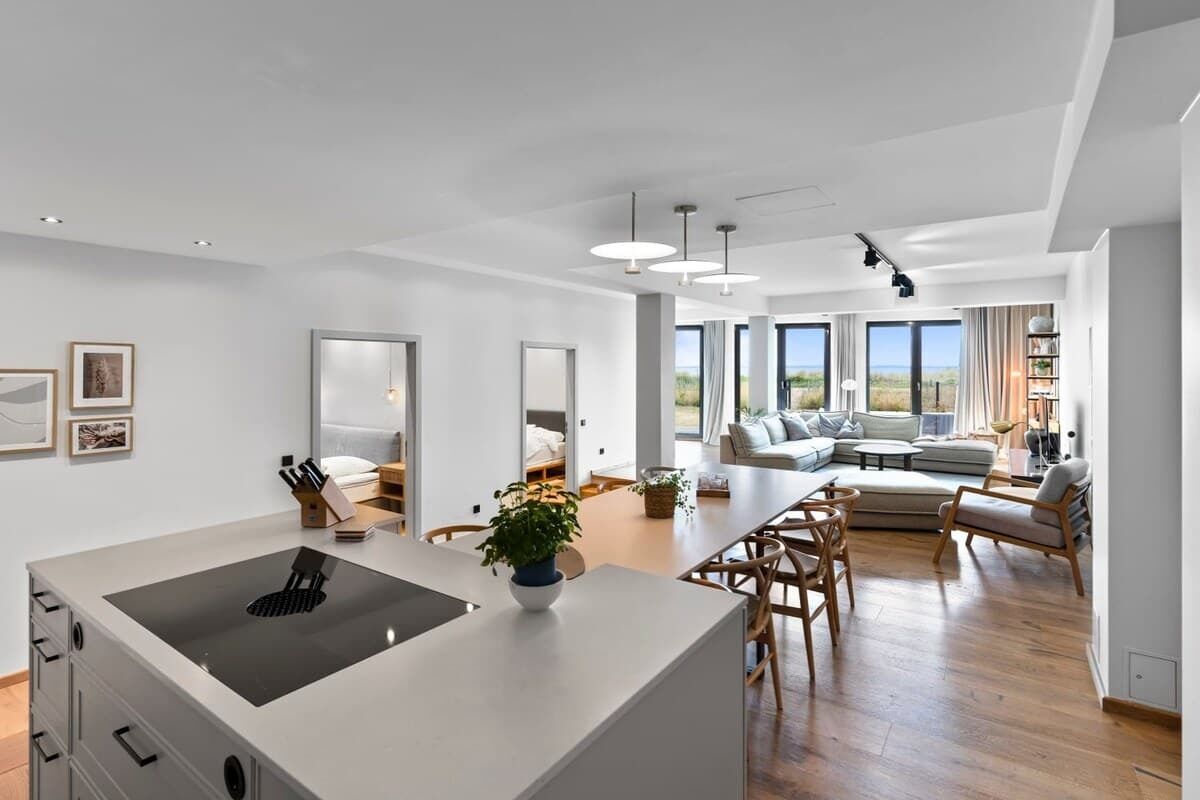 A spacious living area with a large island, wooden flooring, and a view of the outdoors.