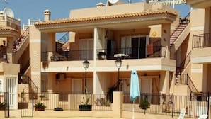 Piscina com espreguiçadeiras e guarda-sóis, rodeada por um edifício com várias andares, varandas e antenas parabólicas.