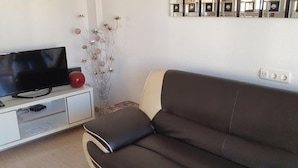 Uma sala de estar com um sofá marrom escuro, um armário branco com uma televisão de tela plana e um vaso decorativo com flores.