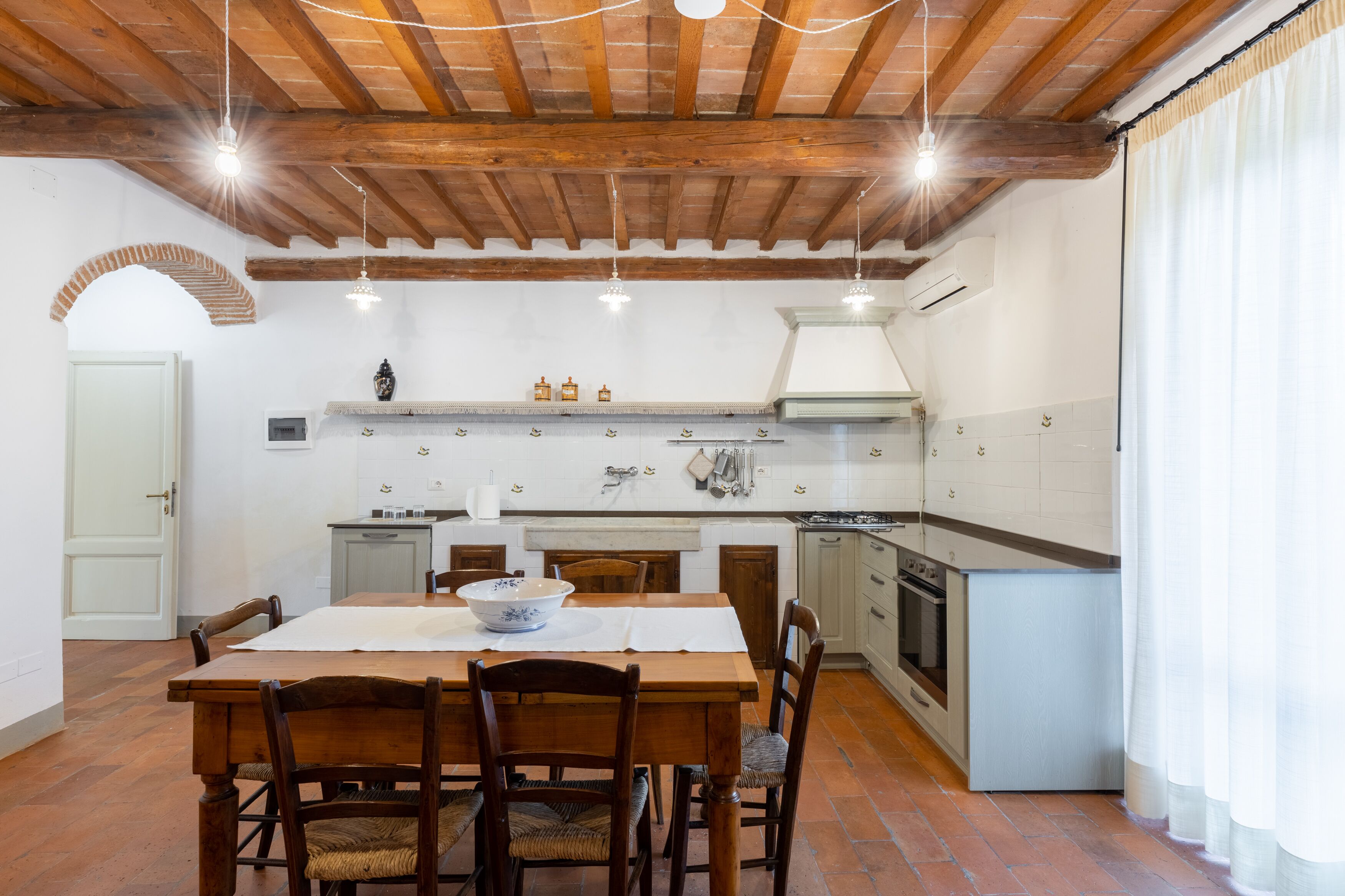 Une cuisine avec une table et des chaises en bois, un plan de travail blanc et un sol en briques.