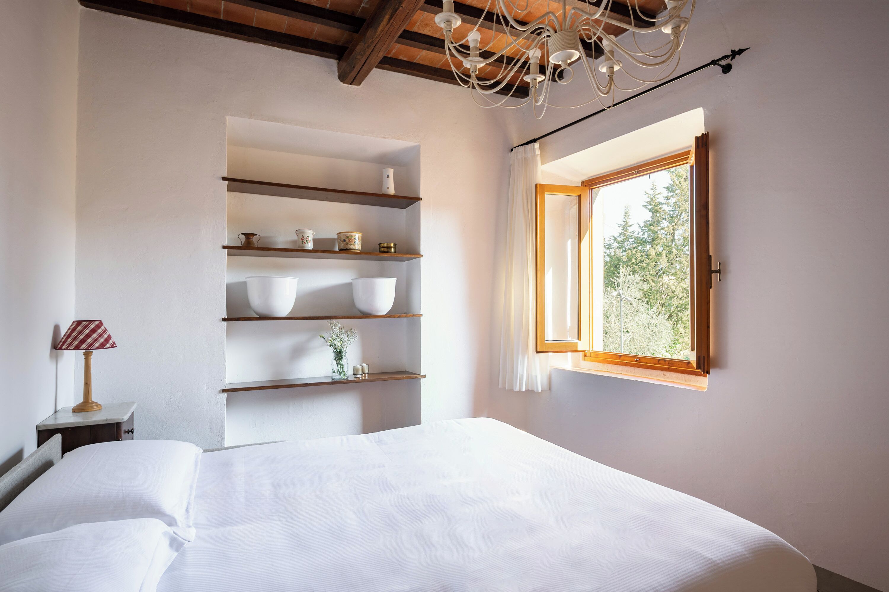 Une chambre à coucher avec un lit, des étagères ornées d’objets décoratifs, une lampe et une fenêtre donnant sur un beau paysage.