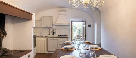 A long dining table set with plates and glasses, a chandelier, and a view into a kitchen area.