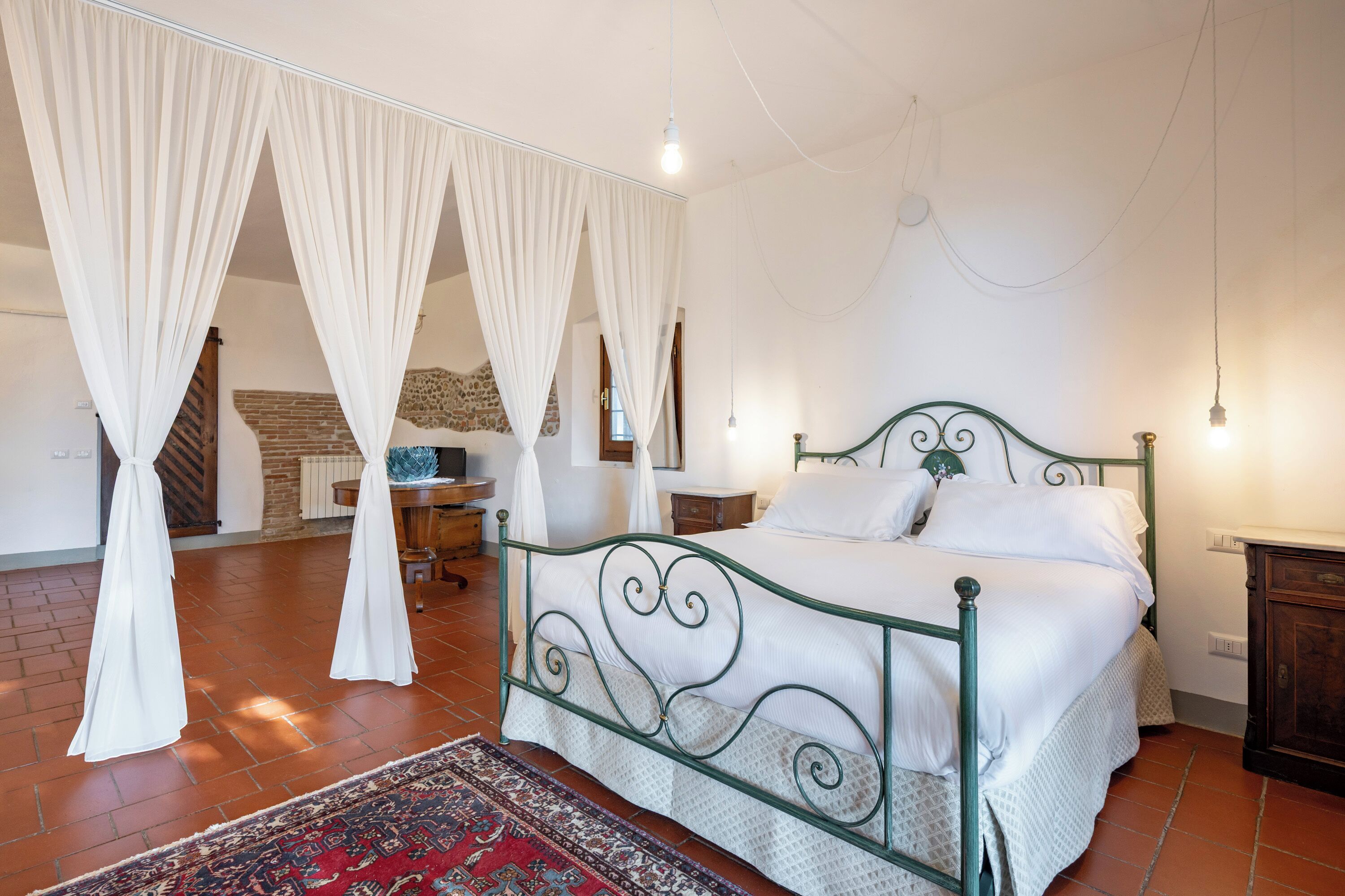 A bedroom with a four-poster bed, a red patterned rug, and a brick floor.
