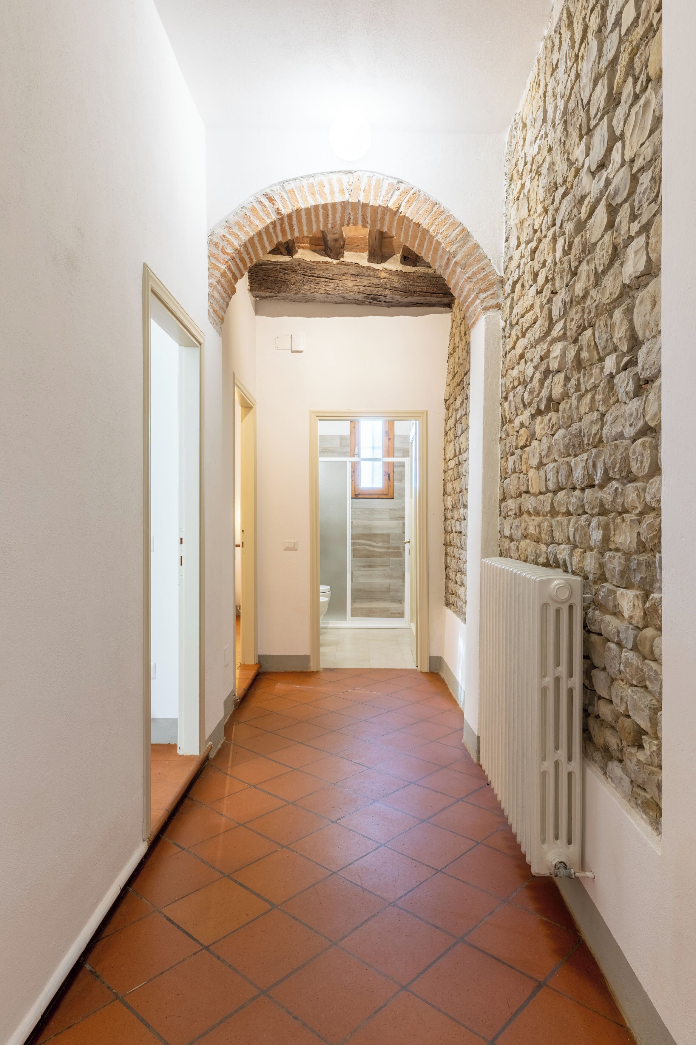 A hallway with a stone wall, a radiator, and a tiled floor.
