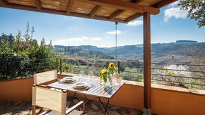 Un área de comedor al aire libre con una mesa lista para dos personas, con vista a un valle pintoresco.