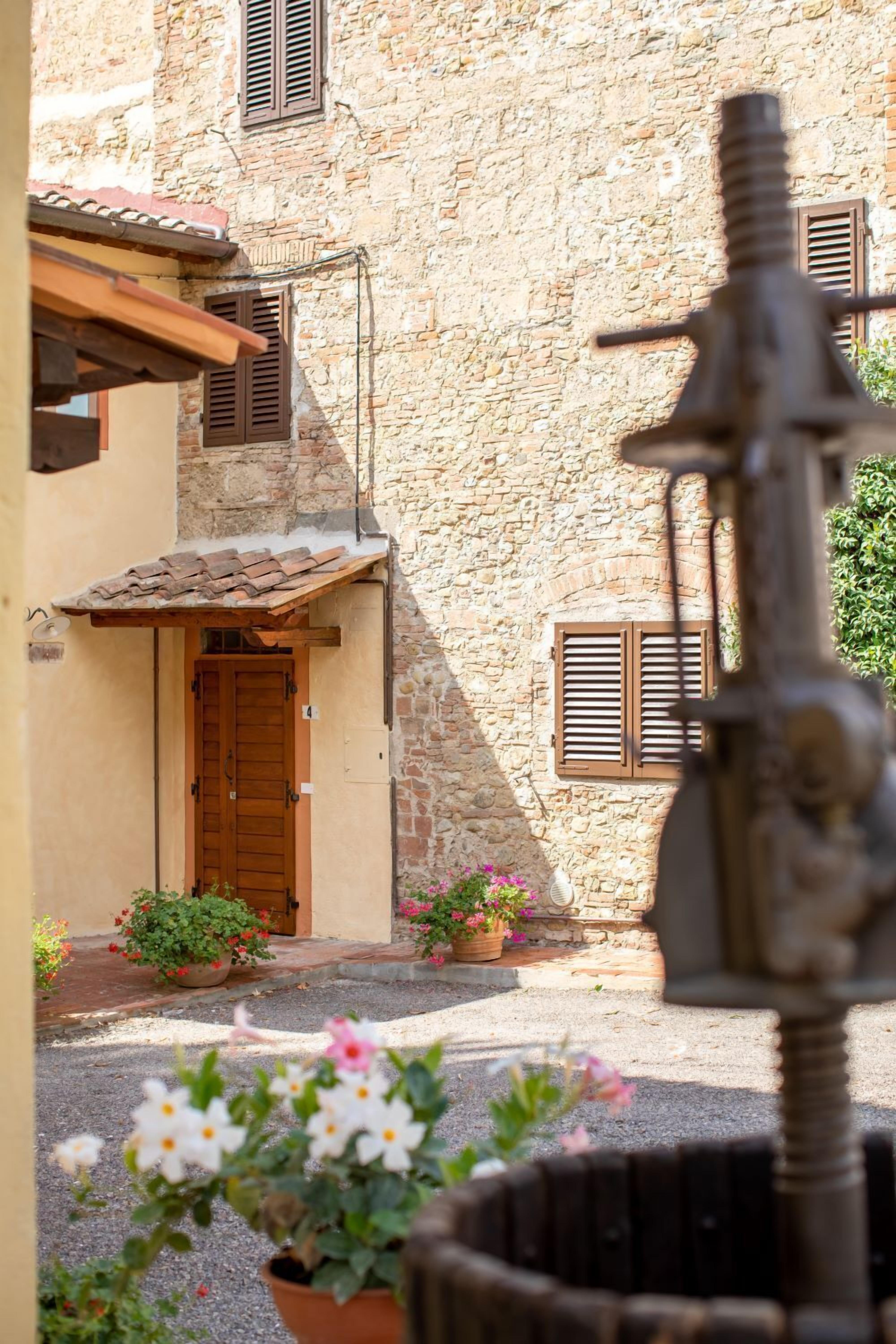 Un cortile con un edificio in pietra, una porta di legno e piante in vaso.