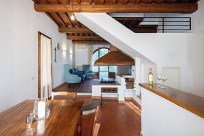Ein Essbereich mit Holztisch und -stühlen, eine Küche mit Kamin und eine Sitzecke mit blauem Sofa.