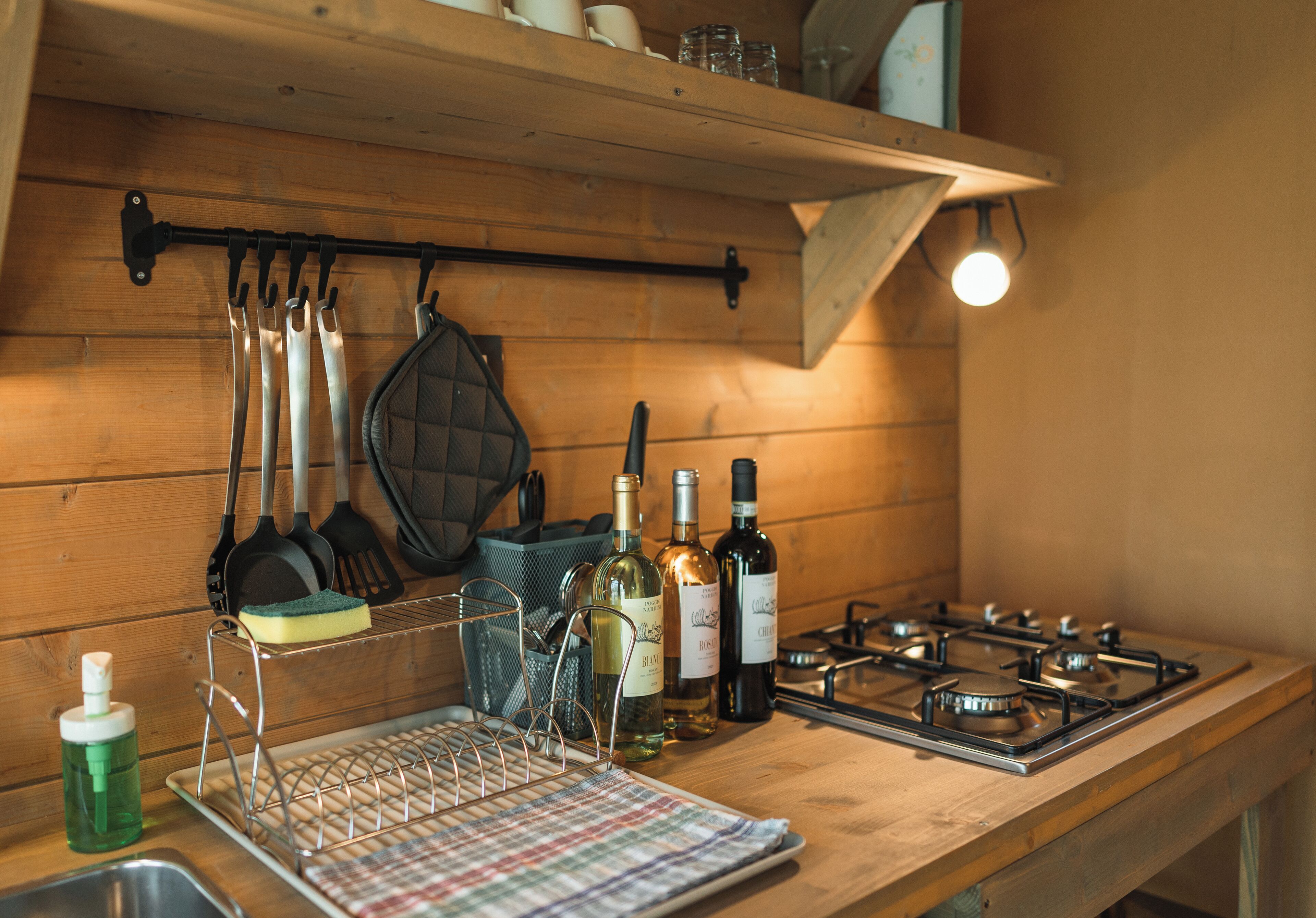 A kitchen with wooden walls, a hanging rack with utensils, a dish rack, and a gas stove.