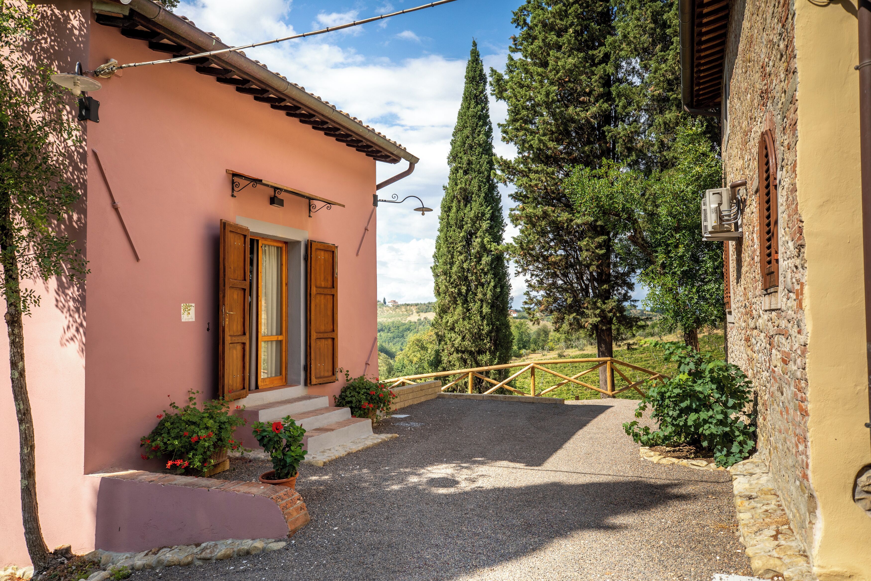 Un edificio rosa con puerta de madera, pared de piedra y camino de grava que lleva a una verja.