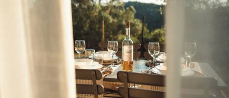 An outdoor dining area with tables set for a meal, a bottle of wine, and glasses on the table.