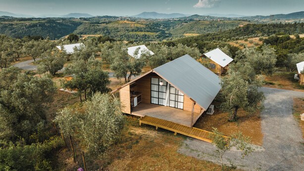 Una cabaña moderna tipo A con un amplio ventanal corredera, rodeada de olivares y con vistas a colinas ondulantes.