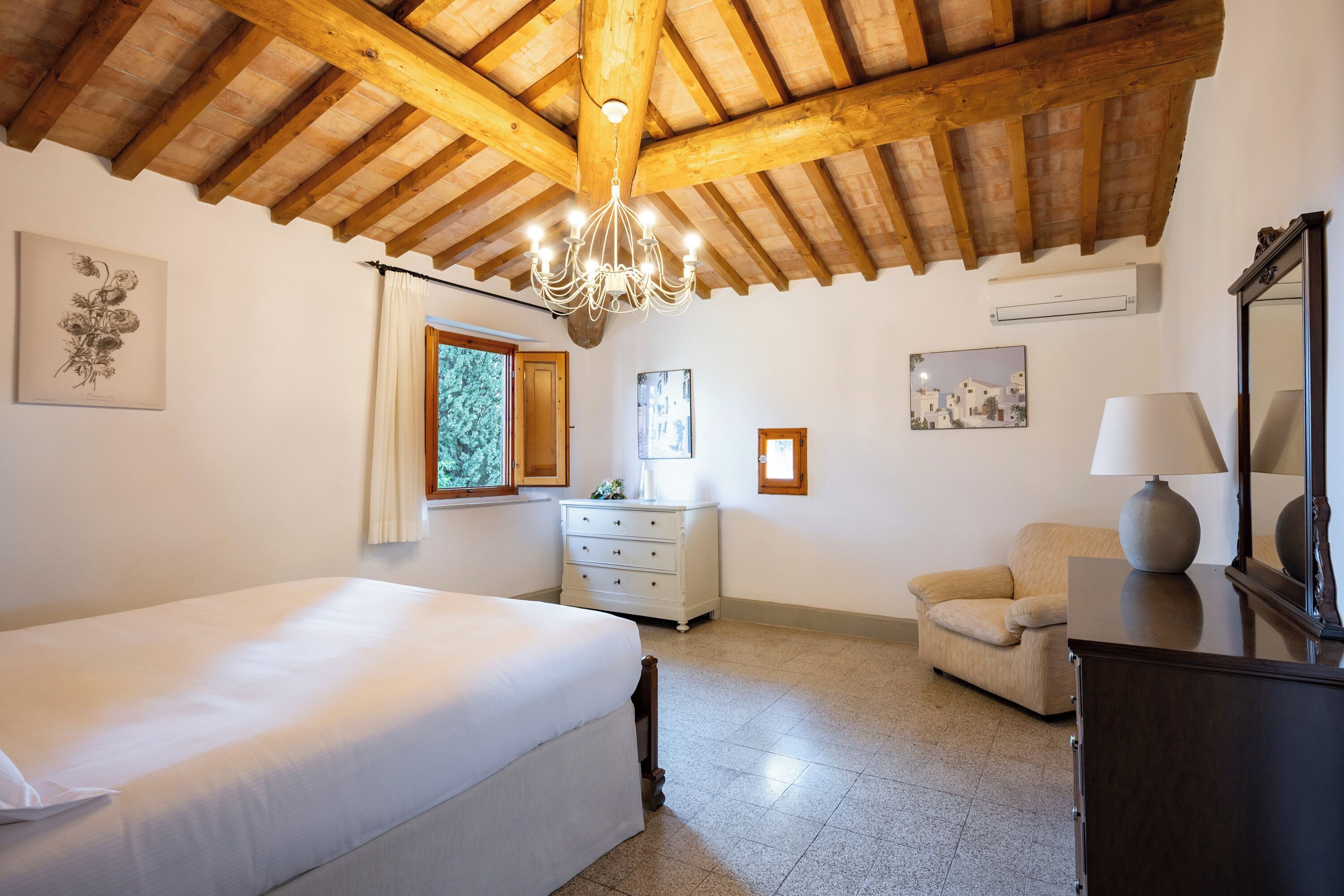 Une chambre avec un plafond en bois, un lit, une commode, une chaise et une lampe.