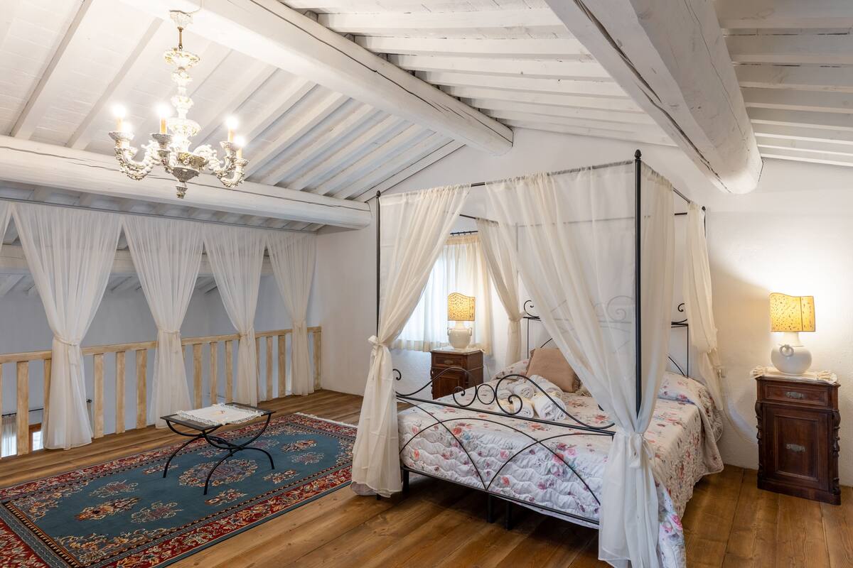 Ein Himmelbett mit weißer Bettwäsche, einer Kristallleuchtre und einem Holzboden.