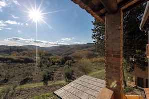 A patio with a view of a hilly landscape, a brick chimney, and a wooden deck. - Agriturismo Poggio Nardini (Montelupo Fiorentino)