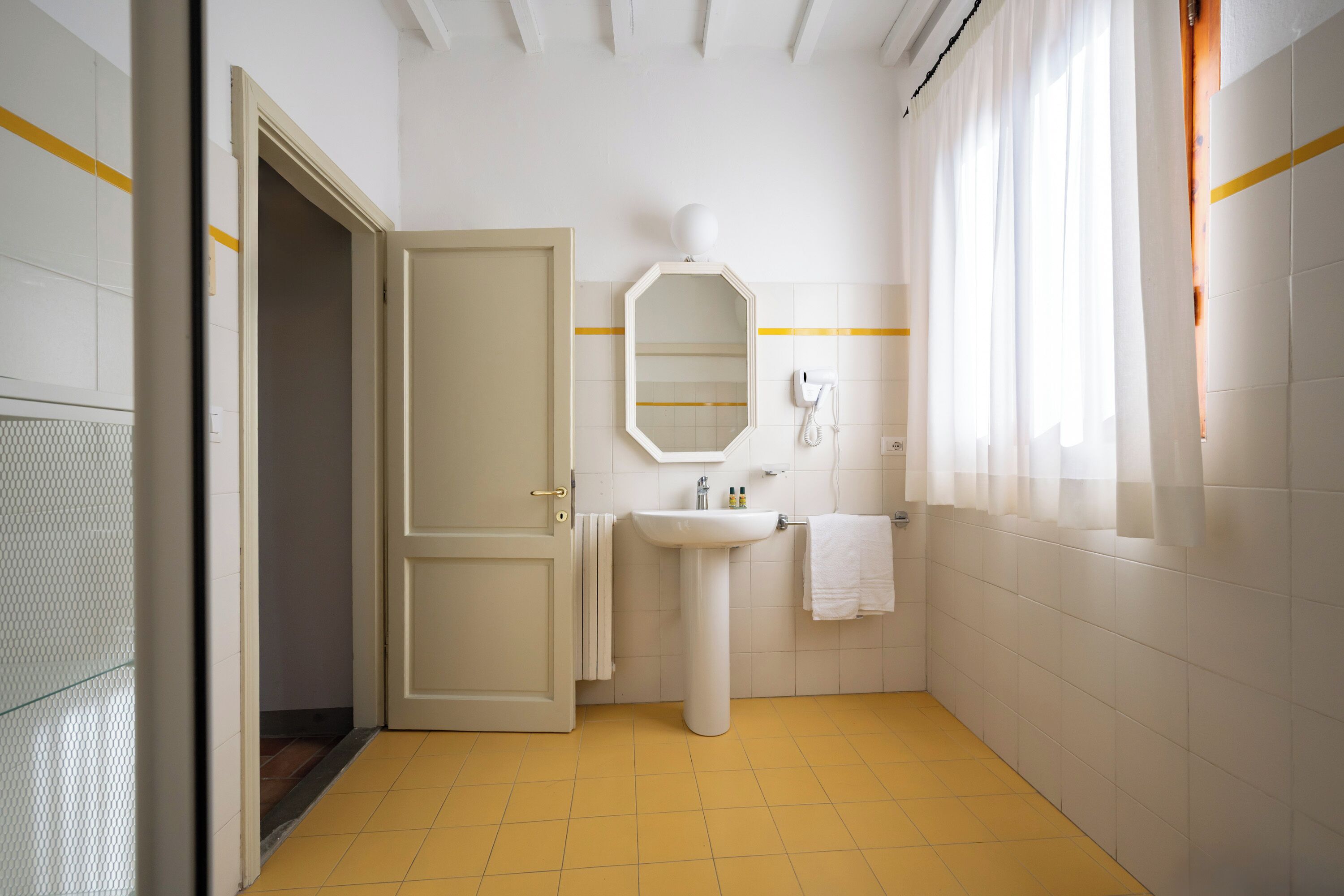 A bathroom with a white sink, a mirror, a towel rack, and a door leading to another room.