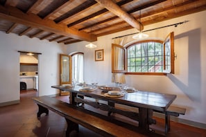 Zona pranzo con tavolo di legno apparecchiato per quattro persone, una panca e vista dalla finestra.