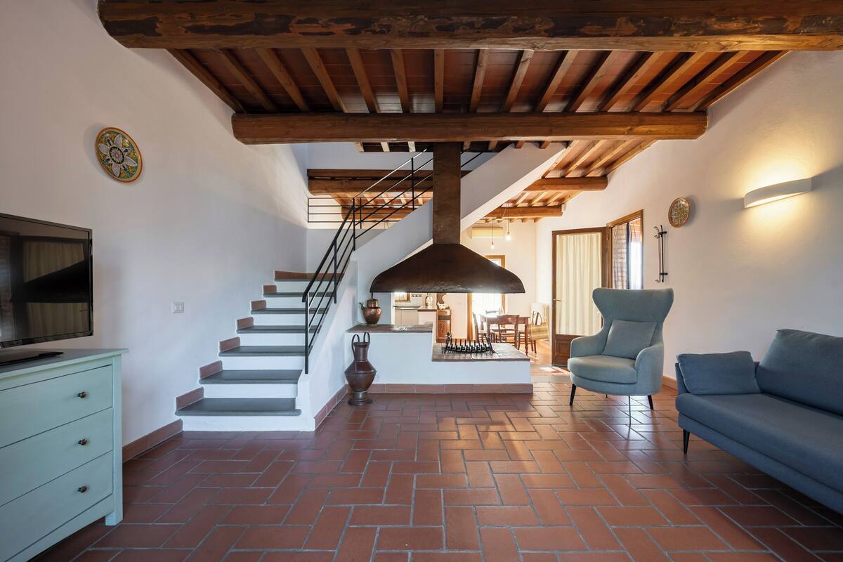 Ein großzügiger Wohnbereich mit Treppe, Sofa, Sessel und Fernseher.