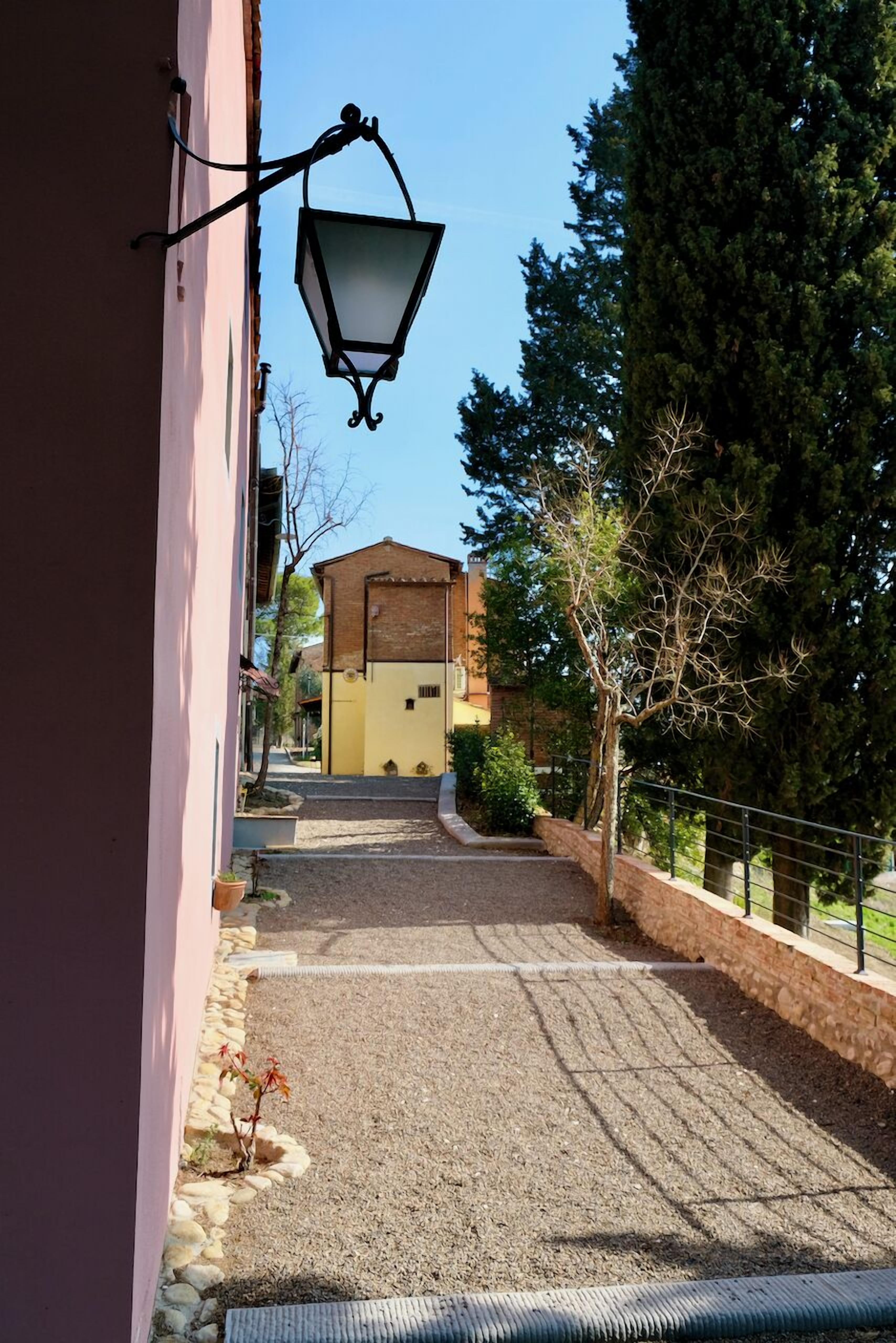 A narrow alleyway with a lamp post, a building entrance, and a tree-lined path.