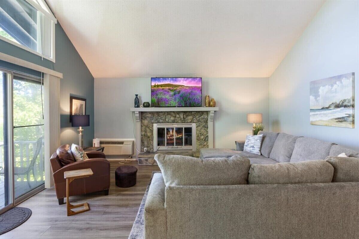 A living room with a fireplace, a sofa, a coffee table, and a television mounted above the fireplace.